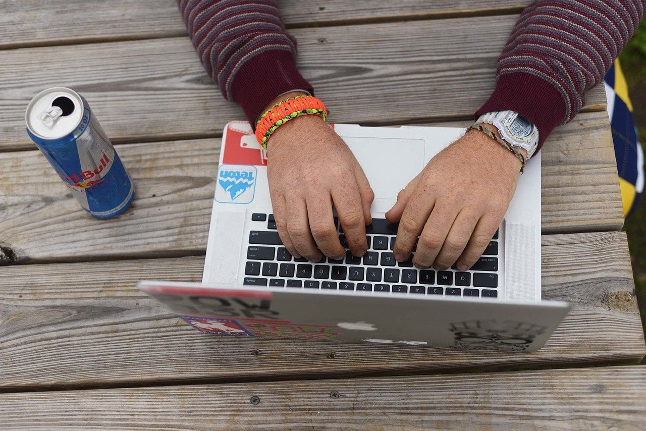 hand typing on laptop with energy drink on the side