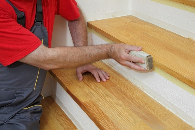 Worker sanding plank at stairs