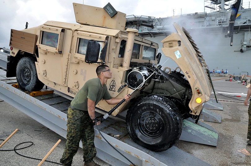 a man pressure washing a military vehicle