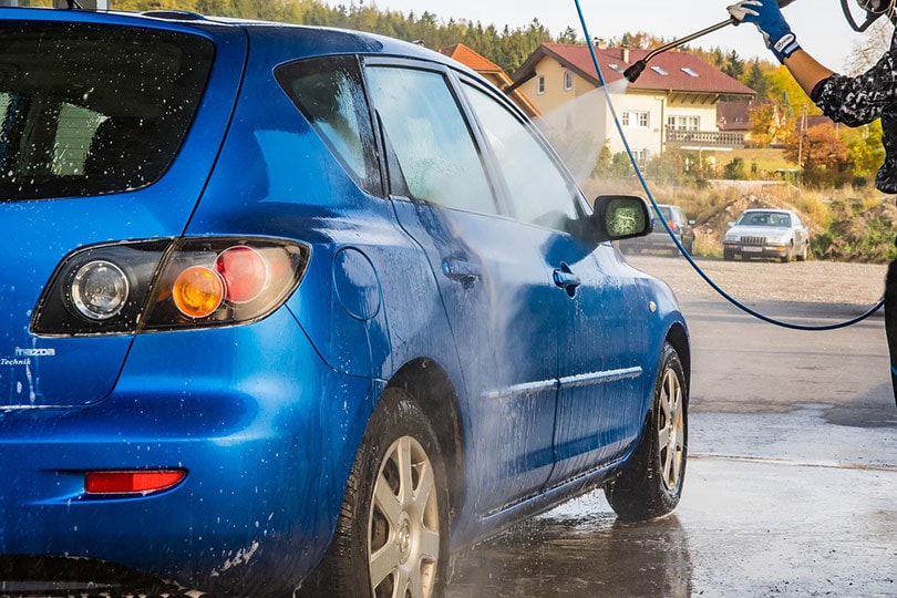 cropped man pressure washing a blue car