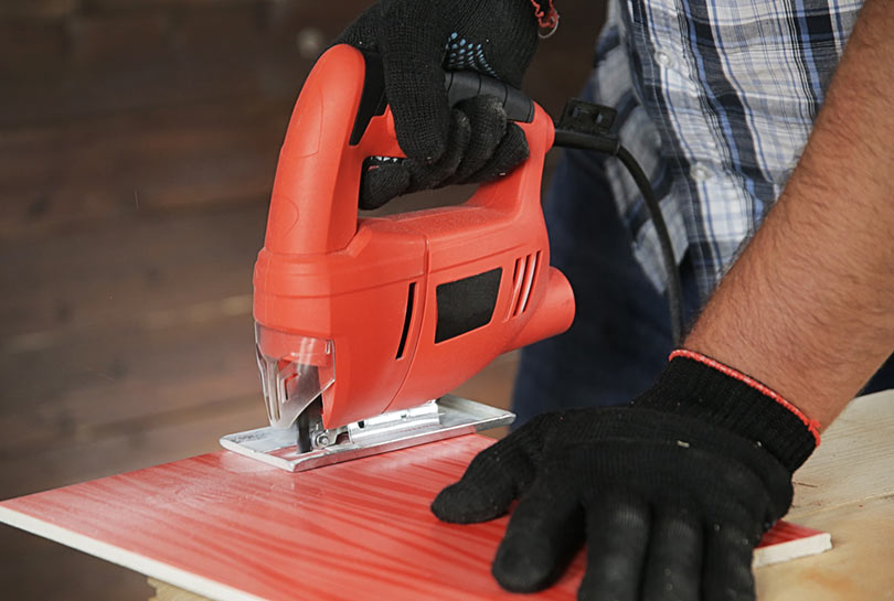cropped man sawing tile with jigsaw