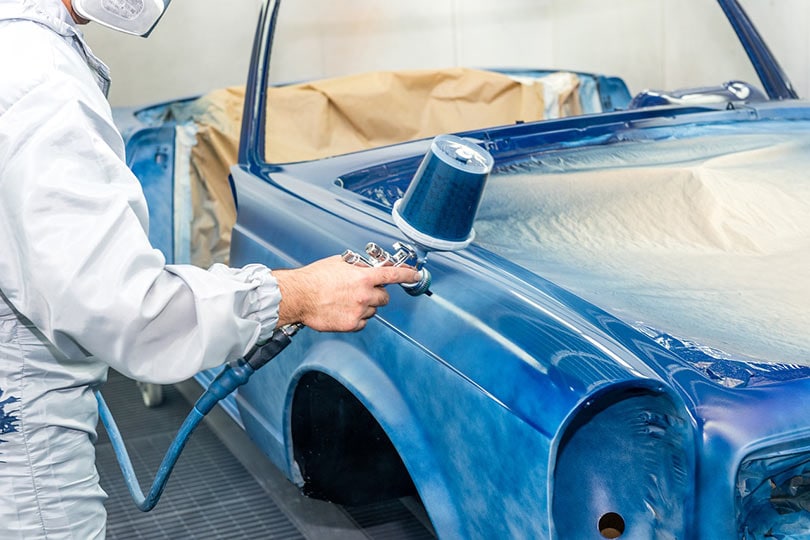cropped man spray painting a car with blue