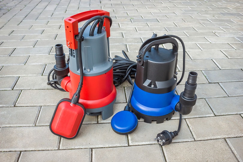two household submersible sump pump with plastic housings on stone floor of courtyard