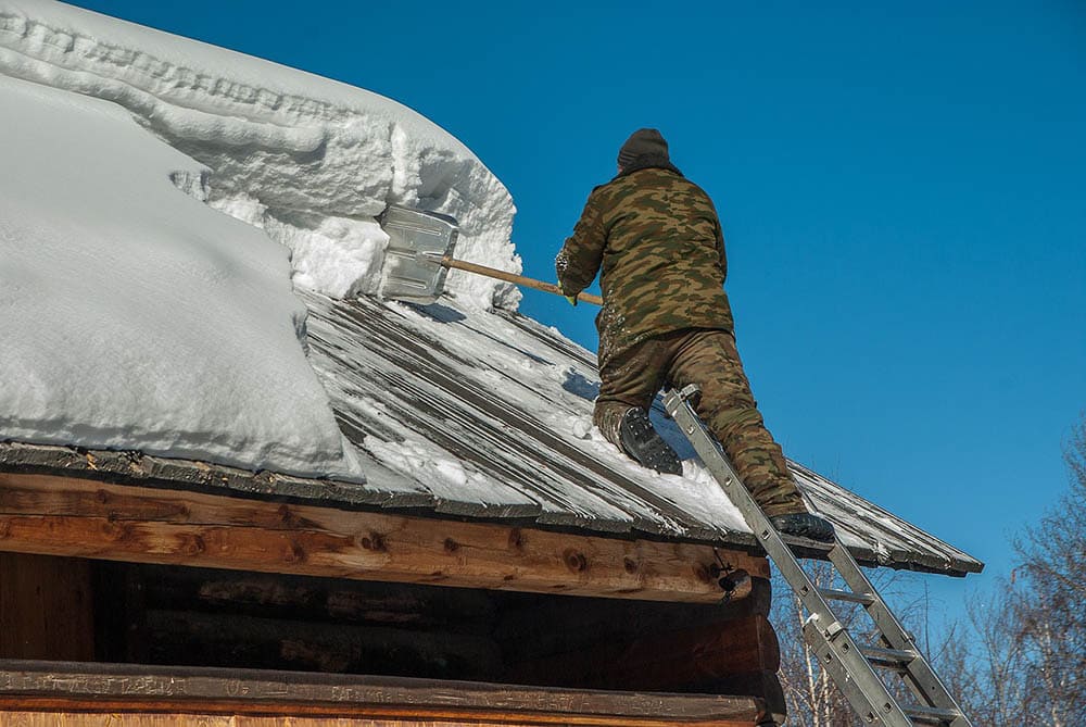 man removing snow on the roof using shovel
