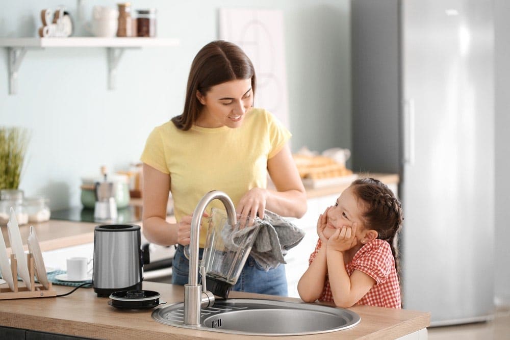 Mother and little daughter cleaning blender in kitchen