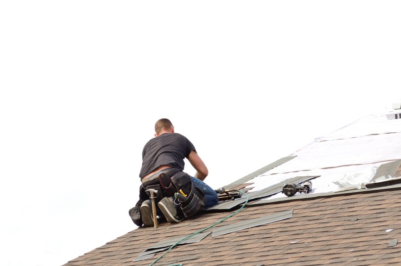 man working on roof shingles
