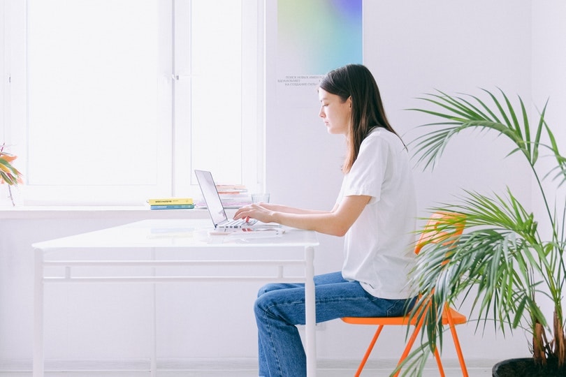 woman in white shirt and demin jeans working on her laptop