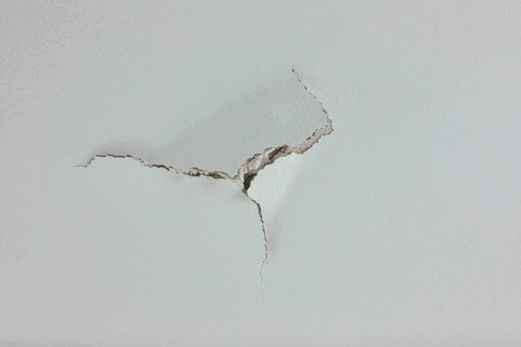 large crack puncture hole in a white ceiling wall. could be a leak and in need of renovation and fixing