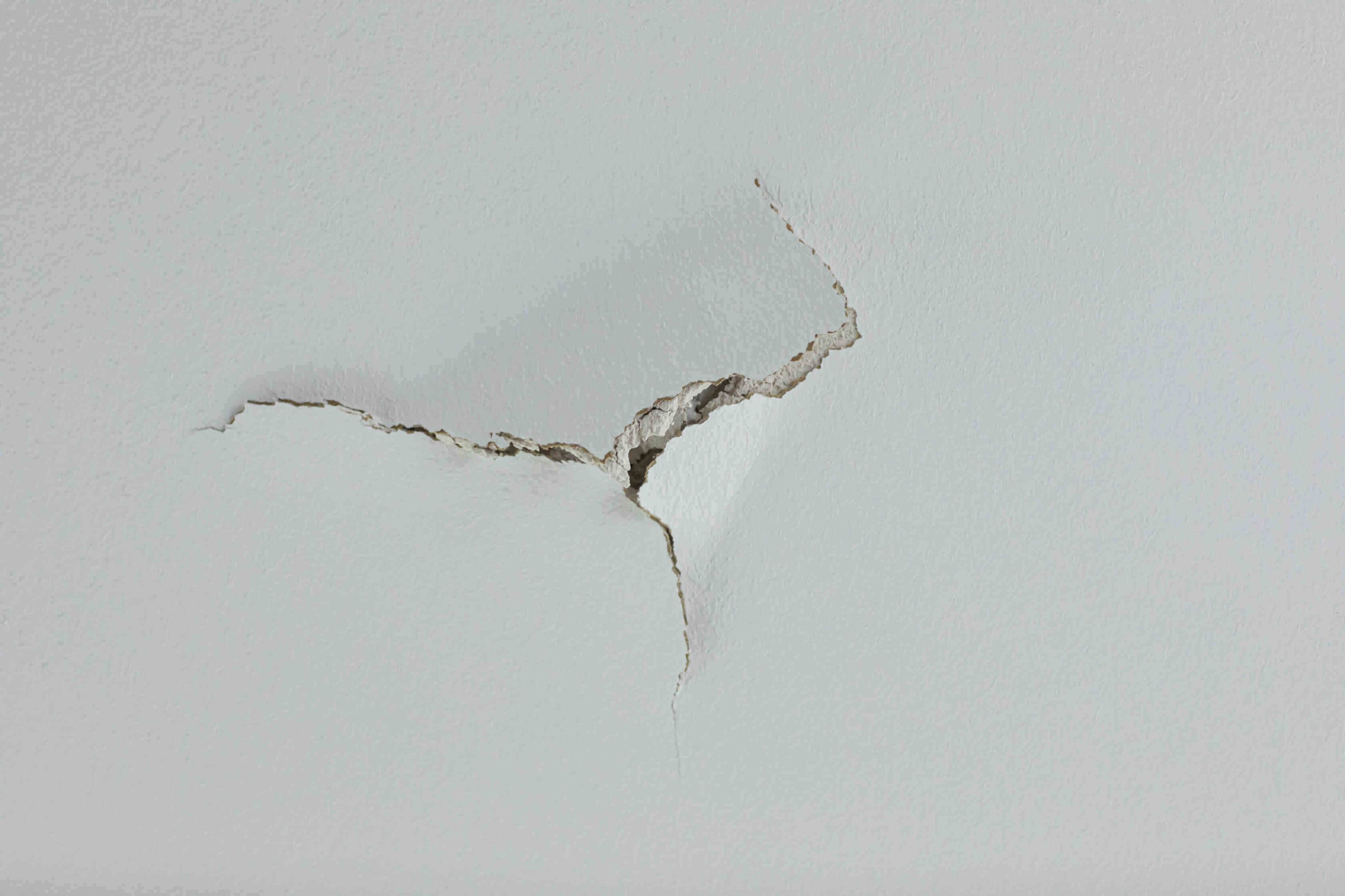 large crack puncture hole in a white ceiling wall. could be a leak and in need of renovation and fixing