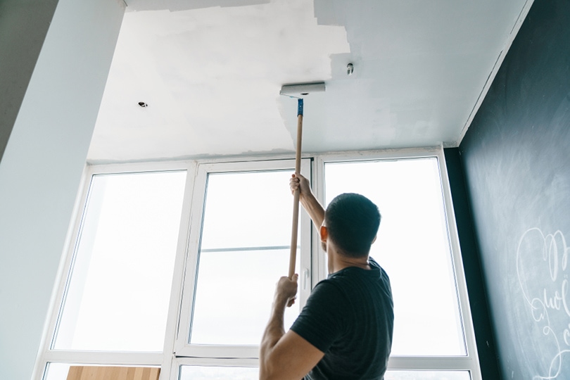 a man painting the ceiling of a room with roller brush