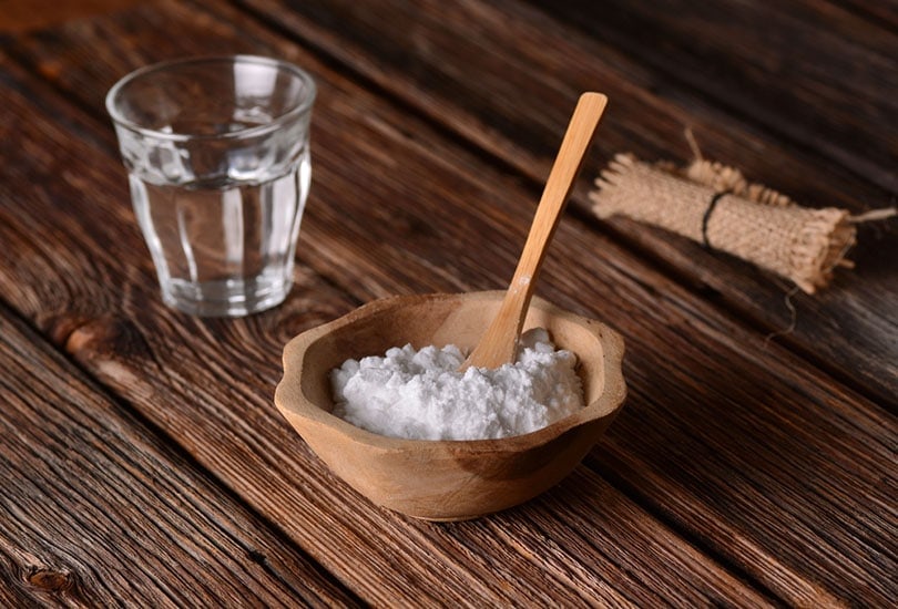 baking soda in wooden bowl with wooden spoon near a glass of water