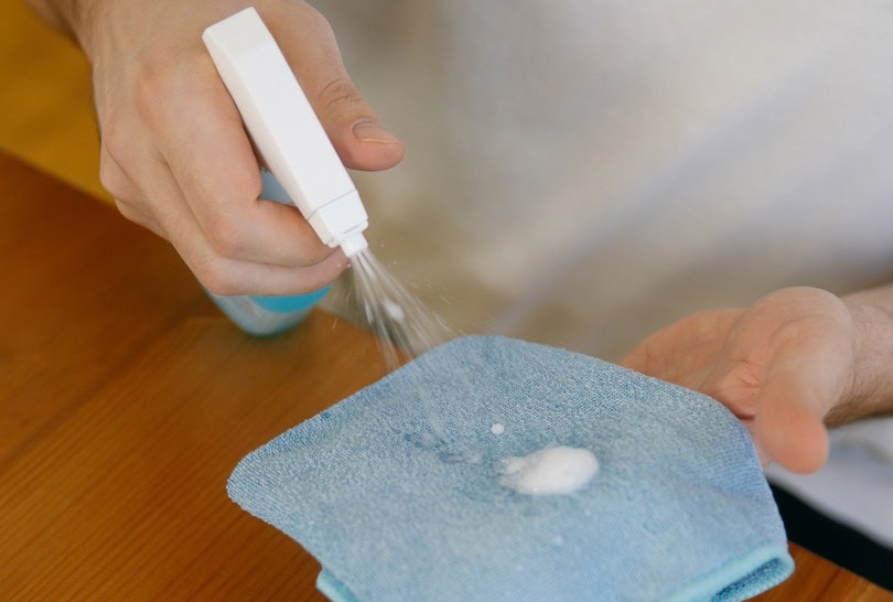 cropped man cleaning wood surface with blue cloth and disinfectant