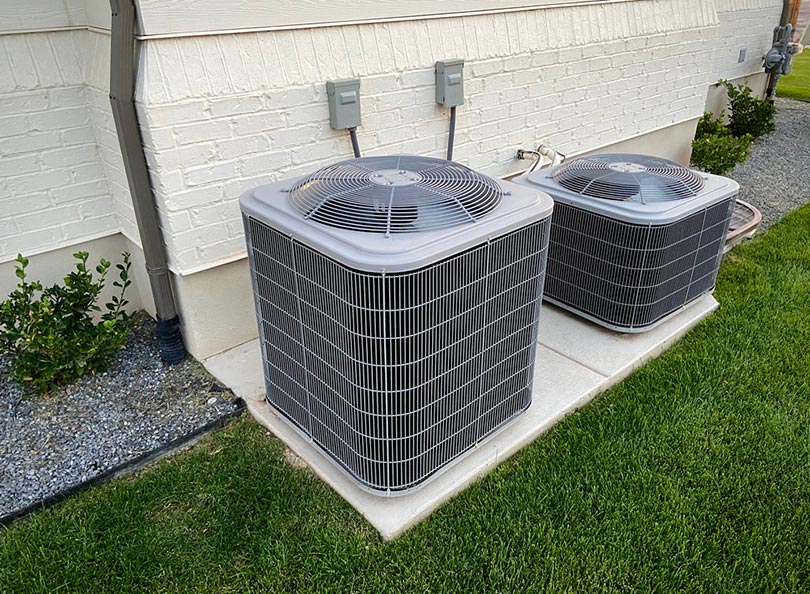 double AC units outside white brick home with green landscape and gravel