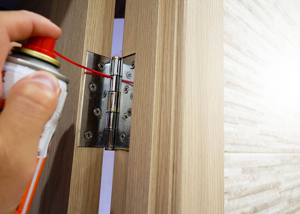 person lubricating door hinge