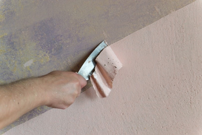 scraping off paint from old concrete wall