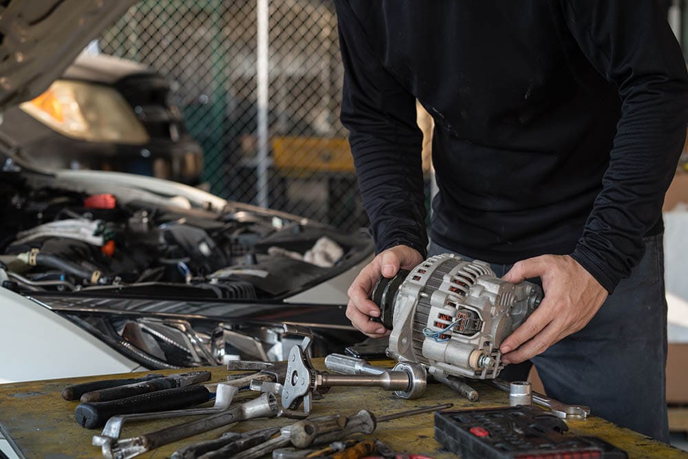 man holding the alternator of the car