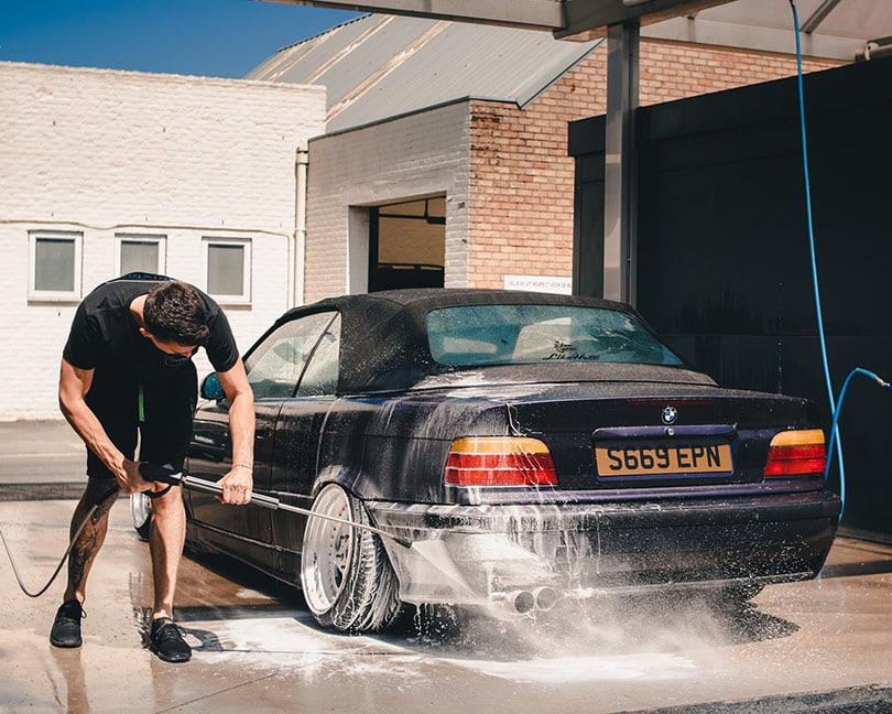 man pressure washing his black car