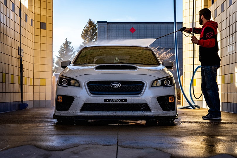 man pressure washing the white car
