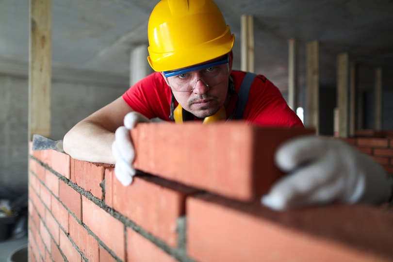 bricklayer carefully puts red brick on the masonry