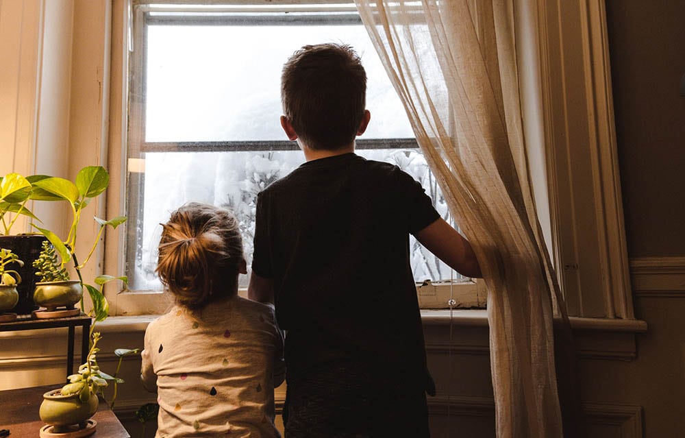 children peeking at the window as the snow falls outside