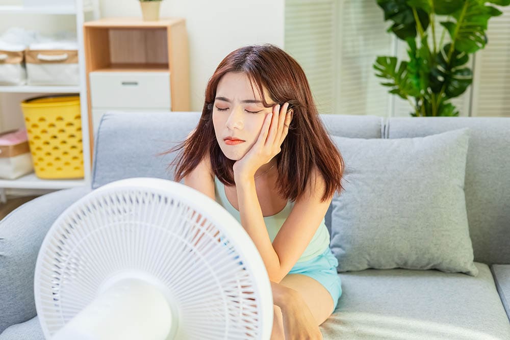 unhappy woman feeling exhausted from heat sitting in front of the electric fan