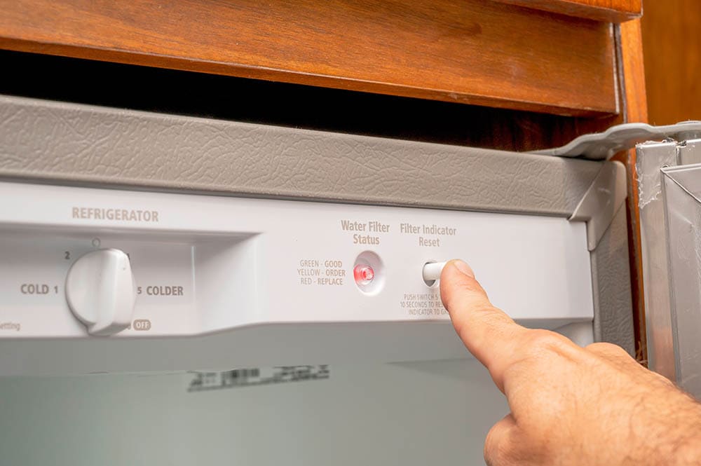 hand pressing fridge water filter button