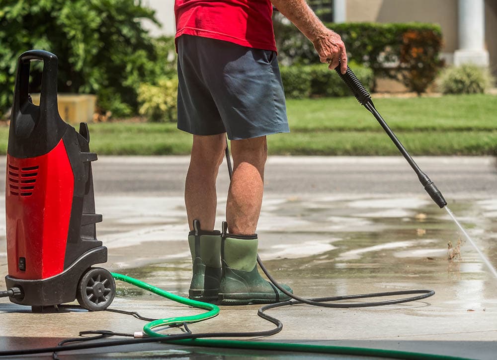 man pressure washing the concrete driveway