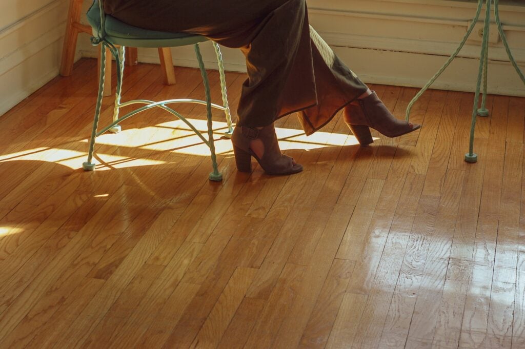 person sitting on a green metal chair on wood floor