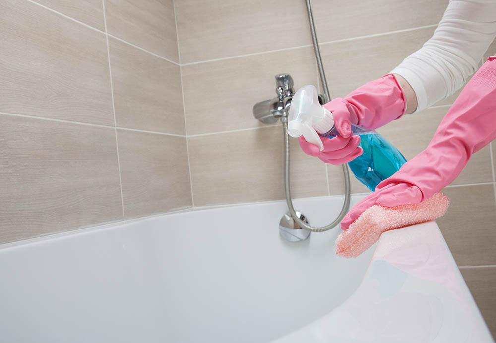 person spraying and scrubbing the bathtub