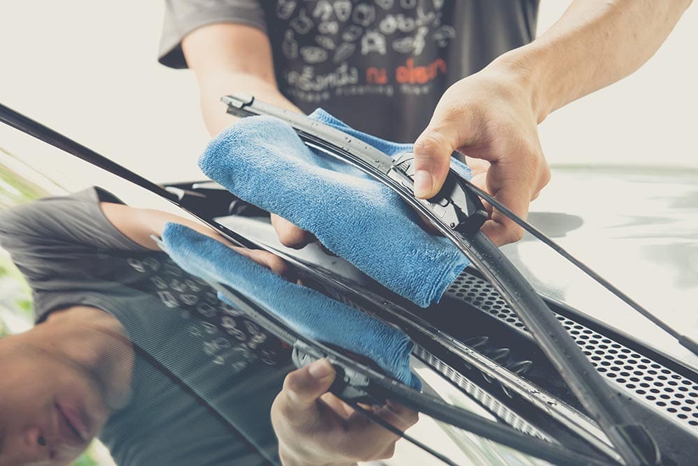 man cleaning windshield wiper with microfiber cloth