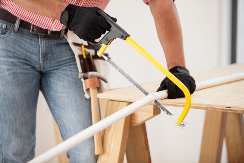 man cutting a pipe with a hacksaw