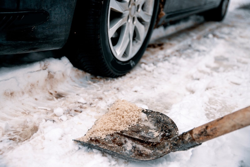 shovel with salt on snowy driveway