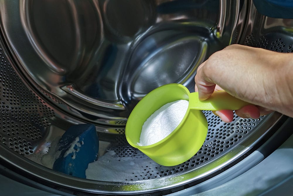 up hand adding baking soda powder in to front-loading washing machine