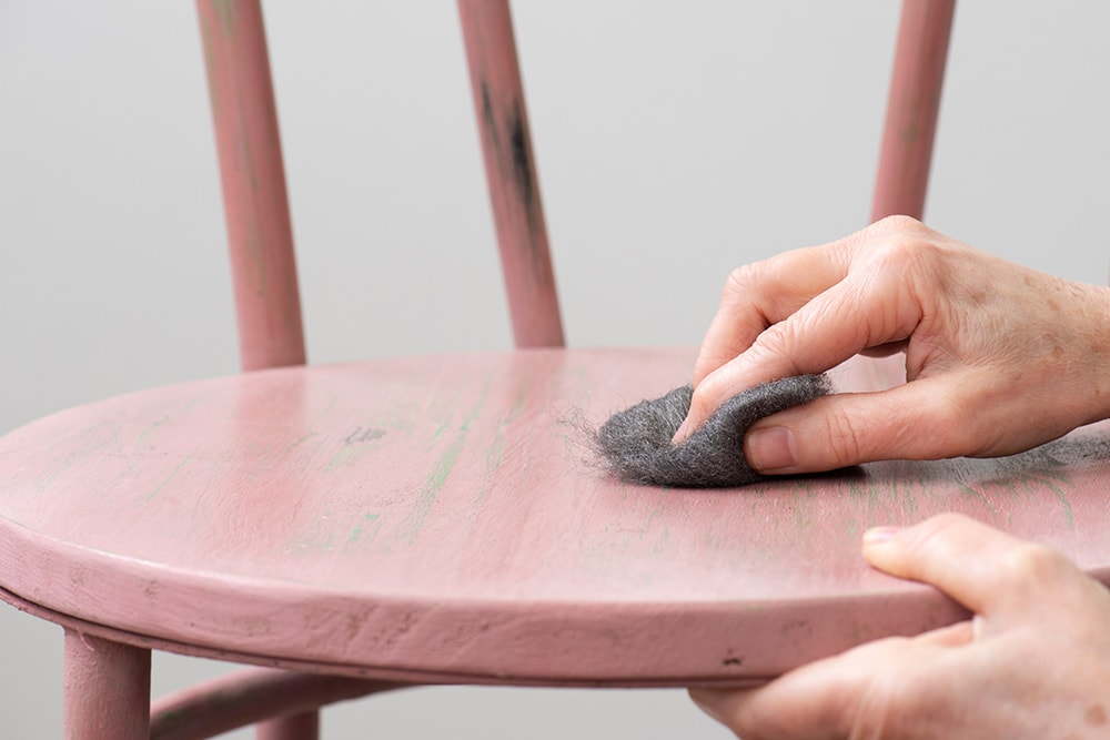 Hand sanding the wooden chair with steel wool