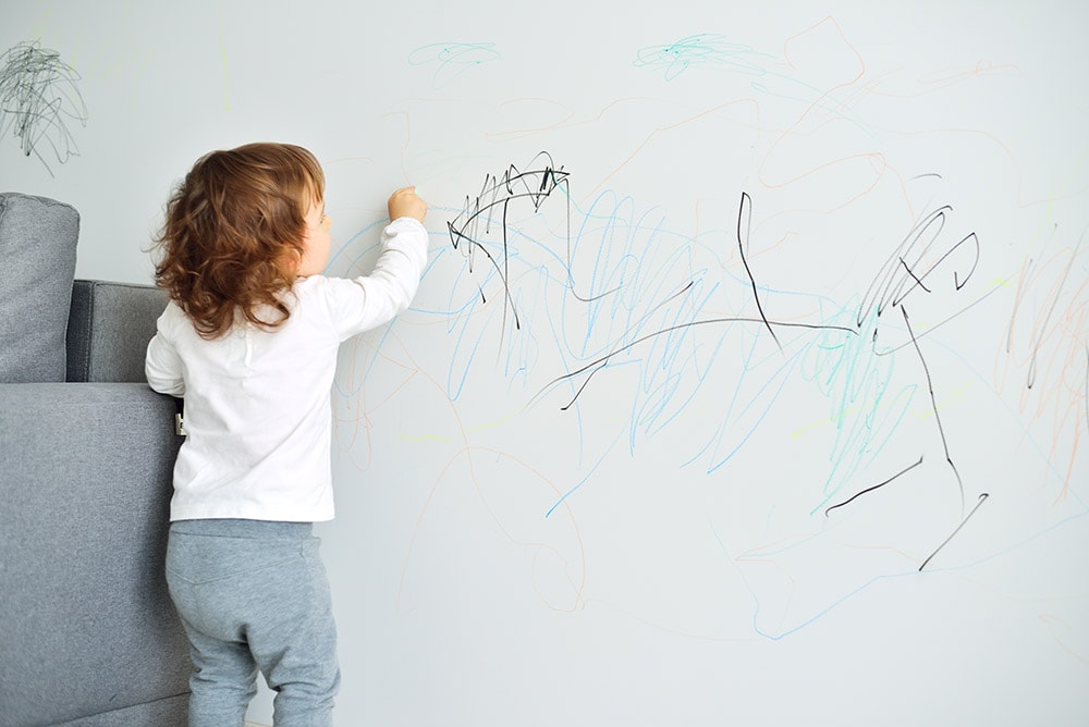little baby girl drawing with crayon color on the wall