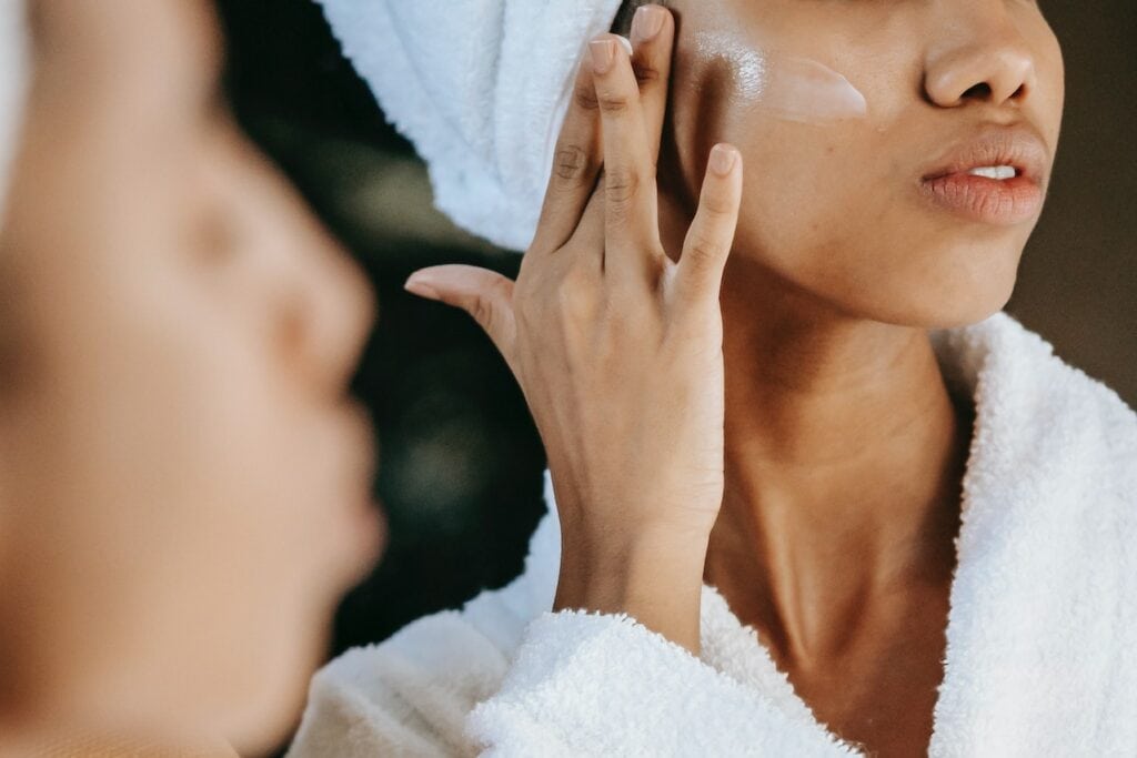 woman applying cream on face against mirror