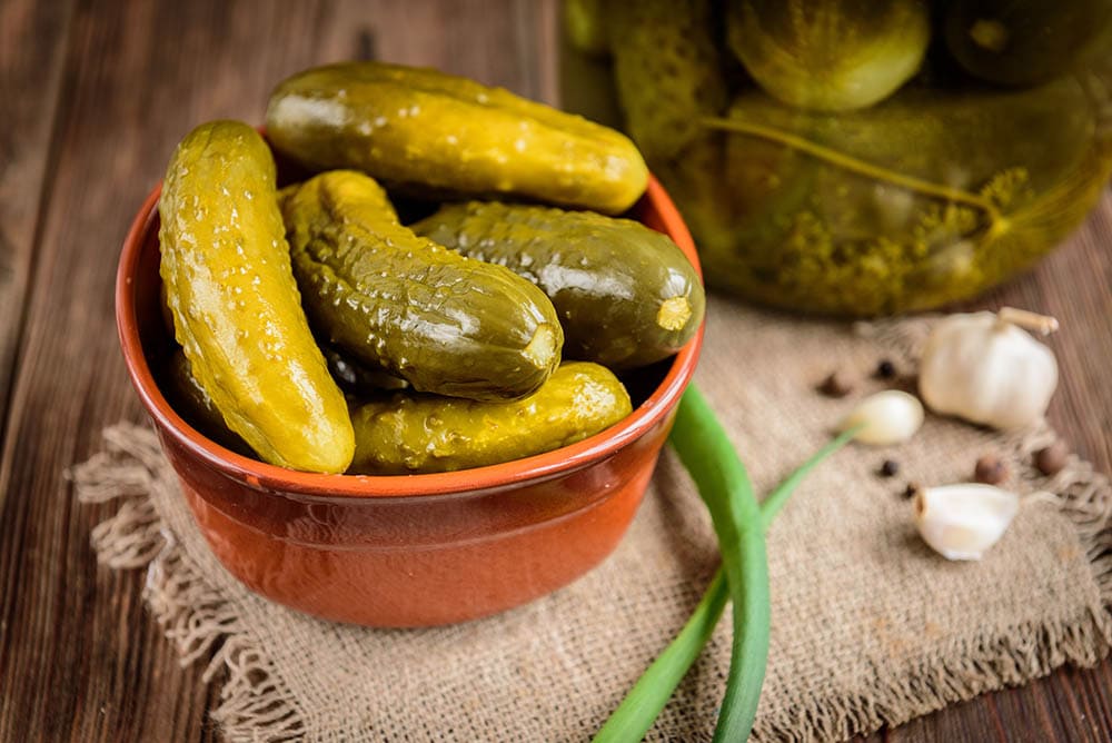 Pickled cucumbers in bowl on wooden rustic table with garlic and jar of pickles