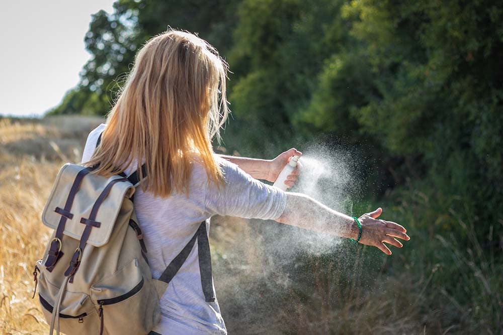 Woman tourist applying mosquito repellent on hand during hike in nature