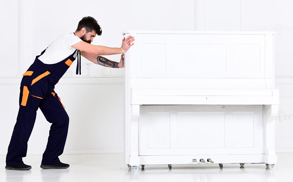 man pushes white piano