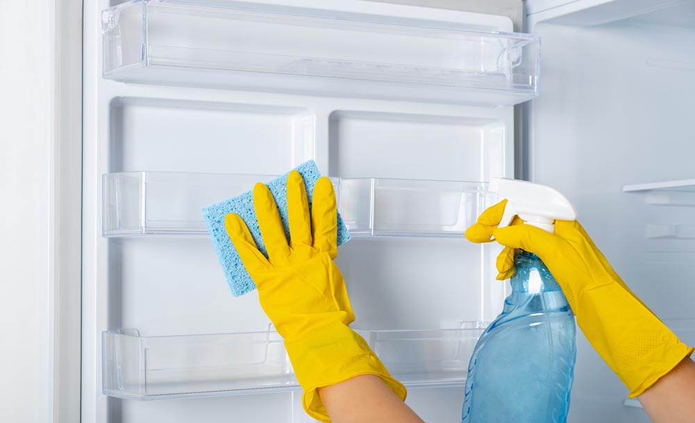 person spot cleaning fridge with a spray