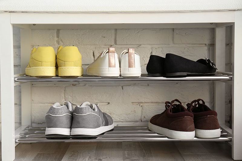 Collection of stylish shoes on rack storage near white brick wall