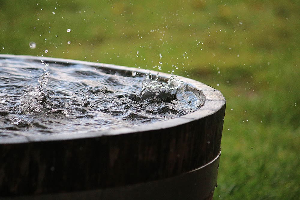 Rain is falling in a wooden barrel full of water in the garden