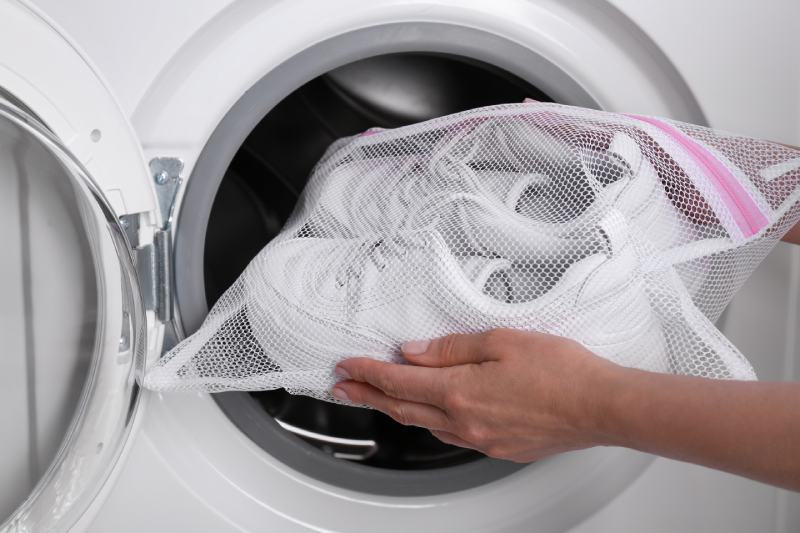 Woman putting pair of sport shoes in mesh laundry bag into washing machine