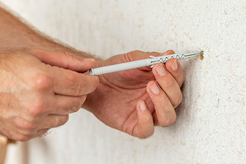 Worker inserts plastic wall plug into a hole