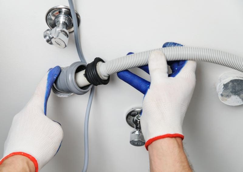Workman attaches a drain hose to a sewage pipe of the washing machine