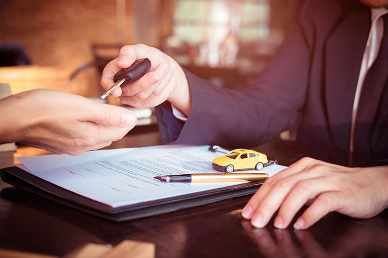 car salesman holding a key with car insurance or warranty