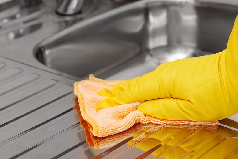 hand in yellow glove wiping stainless steel sink with microfiber cloth