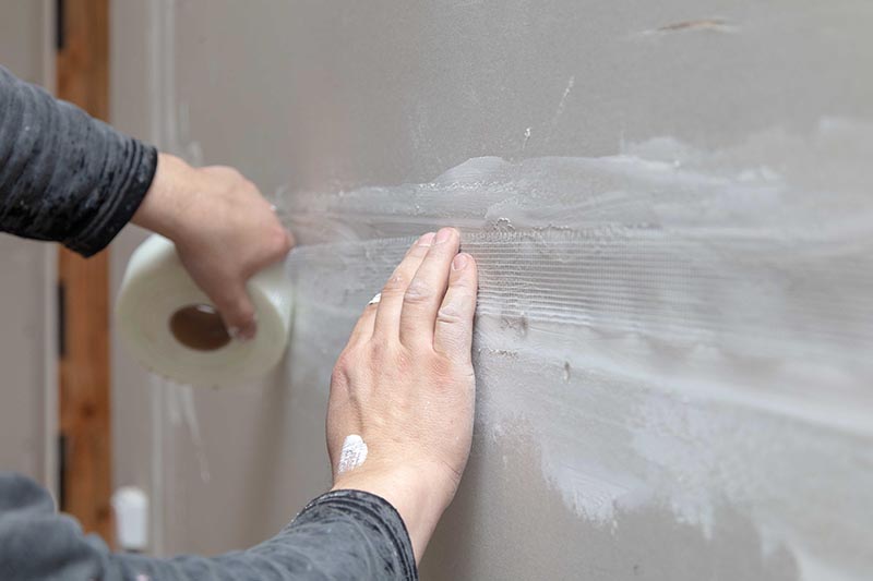 hand putting mesh tape on drywall