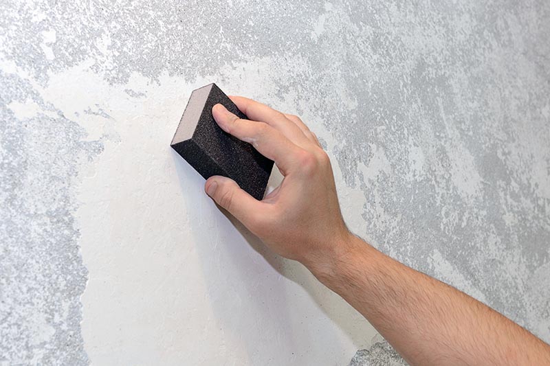 hand sanding wall with sandpaper sponge