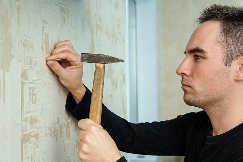 man hammering nail to the drywall